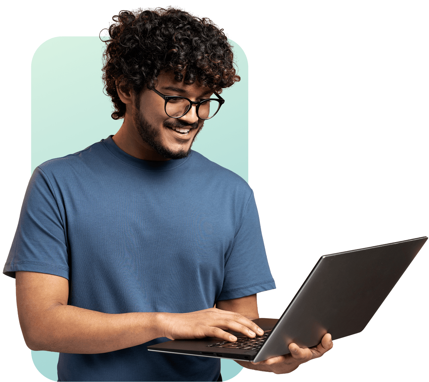 Portrait of a young man with beard, long curly hair and glasses, wearing a blue shirt, smiling confidently while holding a gray laptop against a light and green background.